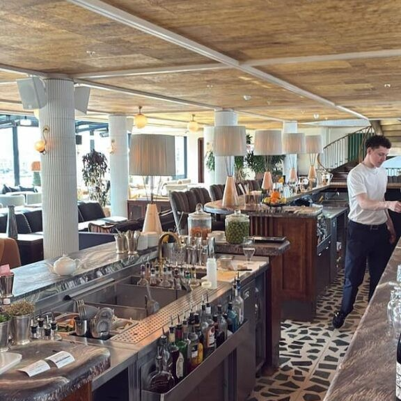 Bar area with black and white flooring and a sink for drinks. White columns and a spiral staircase can be seen in the background.