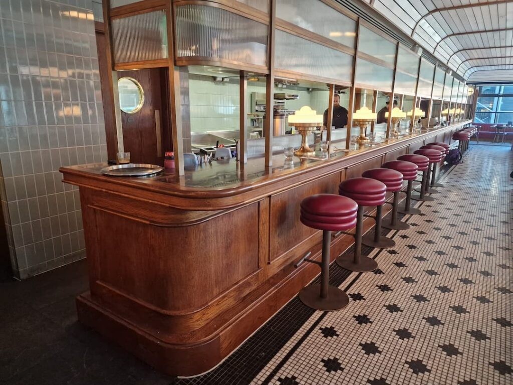 Mollies Diner Bar Area with red diner seats and mosaic tile flooring. There are golden lights on the wooden countertop.